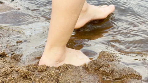 Bare feet walk gently through wet sand and cool water. Video stock 344987774