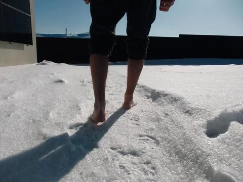 Bare feet walking on fresh white snow with long shadows on a sunny winter day Stock Photos