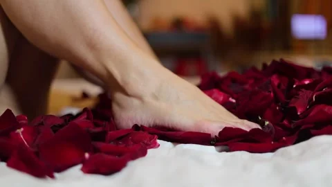 Bare female smooth shaved legs move, wiggle, lift, stir, kick red rose petals Video stock 314505901