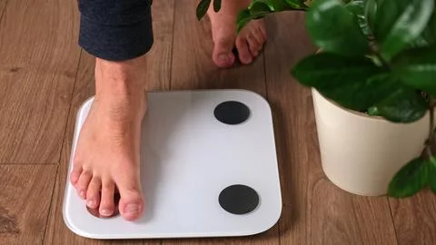Bare foot of man stepping on digital bathroom scale on wooden floor at home.. Stock-Fotos