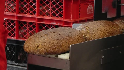 A bare hand steadies a large crusty loaf of dark bread on bakery slicing Stock Footage 335936319