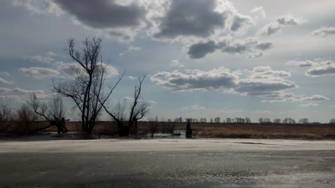 Bare spring trees by frozen river under dramatic cloudy sky Stock Footage 333040235