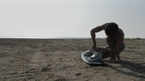 Bare torso guy screws kitesurf boots to board slow motion Stock Footage 118825803