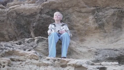 A barefoot blond boy sits on a rock and looks into the distance. Stock Footage 269508046