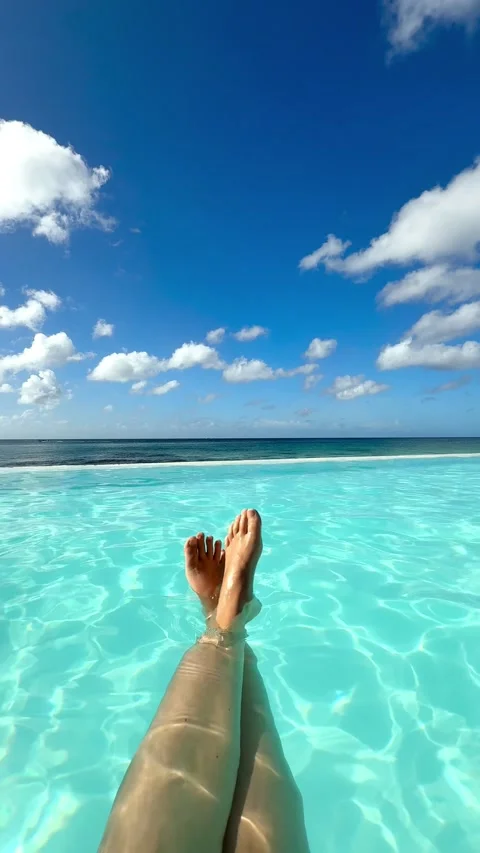 Barefoot in a blue infinity swimming pool on the beach, with blue sky Stock Footage 297612729