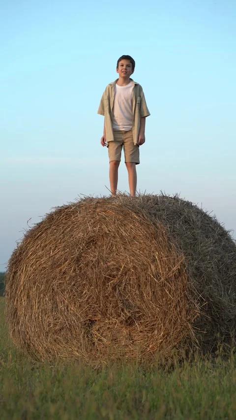 Barefoot boy joyfully jumps high above a large round hay bale  Video stock 342966974