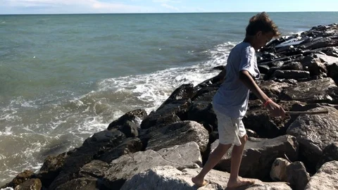 Barefoot boy jumping and running by big stones on sea beach Stock Footage 102340151