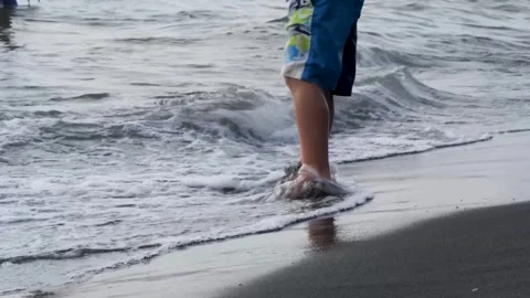 Barefoot kid playing in shallow waves, running along sandy shoreline with joyful Vidéo 301920869