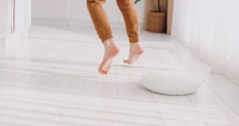 Barefoot legs of a kid running on the white flooring in bright room at home Stock Footage 169256384
