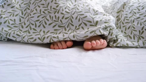 Barefoot. A lying in cozy bed child sticking out his feet from under the blanket Vidéo 305439364