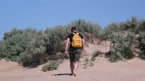 Barefoot man with backpack hiking in beautiful coastal sand dune towards beach Stock Footage 200127539
