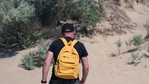 Barefoot man with backpack hiking in coastal hot sand dunes towards beach Stock-Footage 200128653