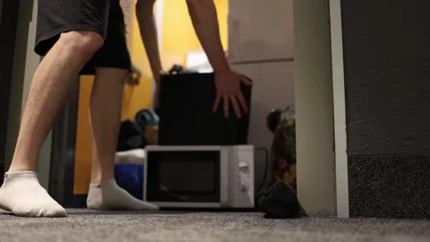 Barefoot man unloading cluttered elevator with microwave box and bags during hec Stock Footage 309331938