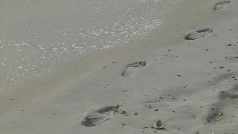 Barefoot prints on white sandy beach with surf gently washing in beside  them Stock Footage 70051340