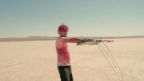 A barefoot red-haired man roams the desert, furiously swinging his guitar, Vídeo Stock 293117525
