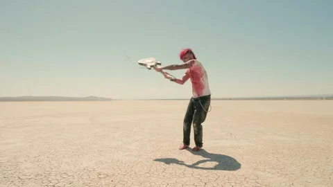 Barefoot red-haired man strides through the desert, angrily swinging his guitar Stock Footage 293117565