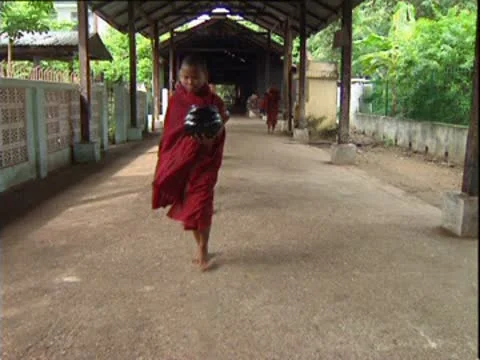 Barefoot, robed young boy monks filing out of Burmese temple to collect alms. Stock Footage 10585333