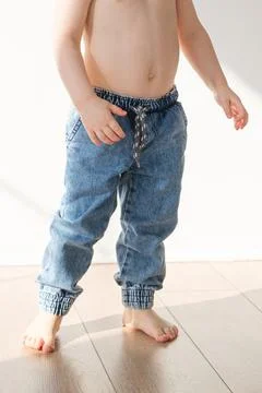 Barefoot toddler boy in elasticated jeans is standing on the floor 스톡 사진