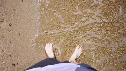Barefoot walking along sandy seashore with gentle waves under bright sunlight Stock Footage 337480322