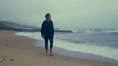 Barefoot  young man walks on the empty ocean beach on the summer cloudy rainy Vidéo 197335964