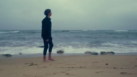 Barefoot  young man walks on the empty ocean beach on the summer cloudy day Stock Footage 197336143