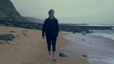 Barefoot  young man walks on the empty ocean beach on the summer cloudy rainy Stock Footage 197336563