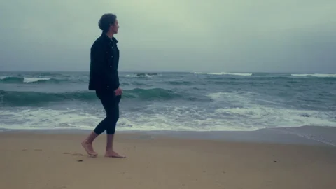 Barefoot  young man walks on the empty ocean beach on the summer cloudy rai.. Stock Footage 254654175