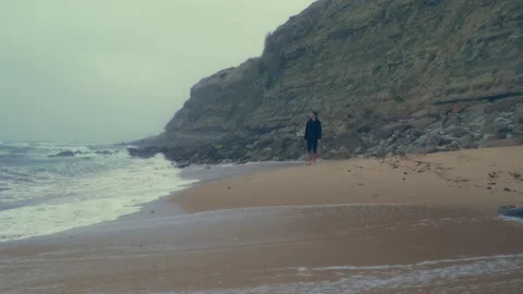 Barefoot  young man walks on the empty ocean sandy beach with big waves. Sa.. Stock Footage 261804376