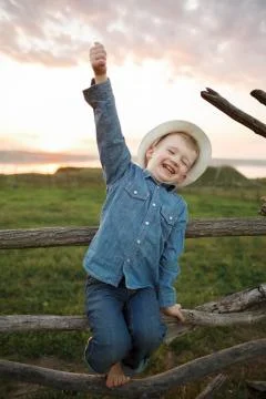 Barefooted boy in a hat makes faces on the farm posing at the camera Stock Photos