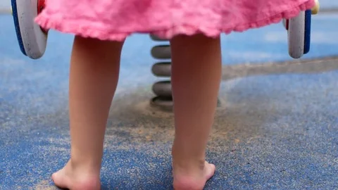 Barefooted child on the playground. The girl is standing near the swing. We see Stock Footage