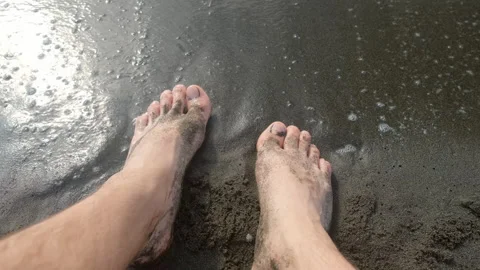 Barefooted man legs on sandy volcanic beach: gentle waves washing over feet. Stock Footage 311471736