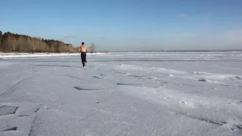 Barefooted man with a naked torso running across the ice of a frozen river Stock Footage 82887789