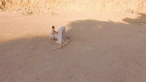 A barefooted man in white clothes plays the piano among the yellow mountains. A Stock Footage 94257192