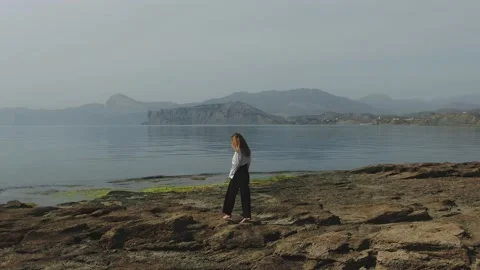 A barefooted young lady is walking along a rocky cape. She easily jumps from Stock Footage 147432670