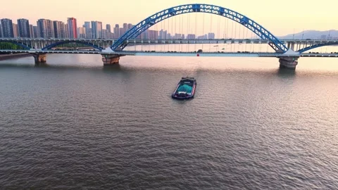 Barge navigating under a modern blue bridge at sunset with city skyline in the Stock Footage 308844019