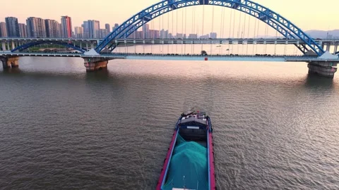 Barge navigating under a modern blue bridge at sunset with city skyline in the Stock Footage 308844446