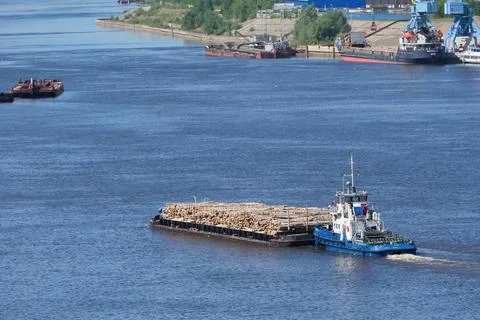 A barge unloaded with large logs goes along the river in summer. Stock Photos