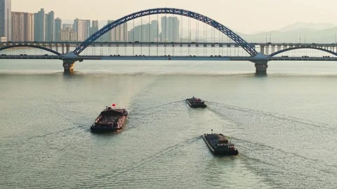 Barges navigate the river under a modern bridge in a city skyline view at Stock Footage 310117451