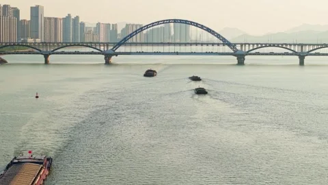 Barges navigate the river under a modern bridge in a city skyline view at 스톡 동영상 311559574