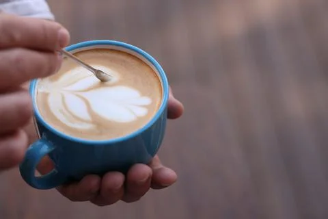 Barista creating pattern in cup of coffee on blurred background, closeup. Spa Stock Photos