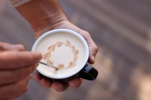Barista creating pattern in cup of coffee on blurred background, closeup. Spa Stock Photos