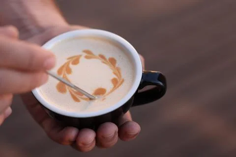 Barista creating pattern in cup of coffee on blurred background, closeup. Spa Stock Photos