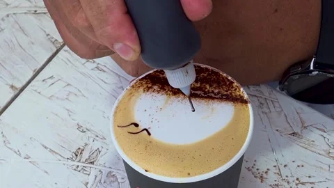 Barista drawing face pattern with chocolate syrup on a cappuccino milk foam  Stock Footage 347620229