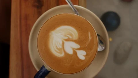 A barista gently sets a freshly made cappuccino with smooth latte art on a Stock Footage 325077786