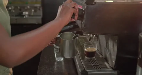 Barista hands are reaching for control knob and steaming milk pitcher at Stock-Footage 344105104