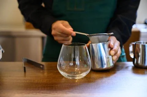 Barista preparing coffee drink using sieve and pitcher on counter Фото