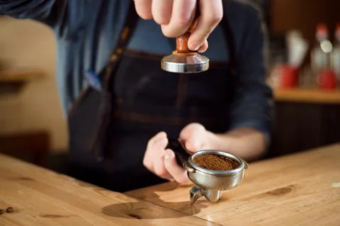 Barista presses ground coffee using tamper in a coffe shop Stock Photos