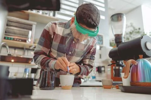 Barista in protective visor making pattern on coffee Stock Photos