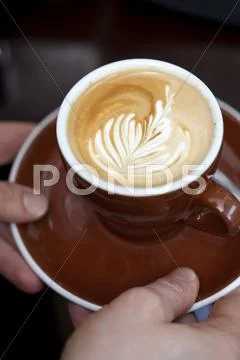 A barista serving a cappuccino with a floral pattern in the milk froth Stock Photos