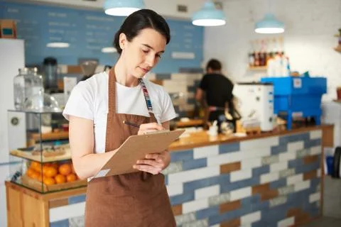 Barista standing while writing in the notepad. Stock Photos